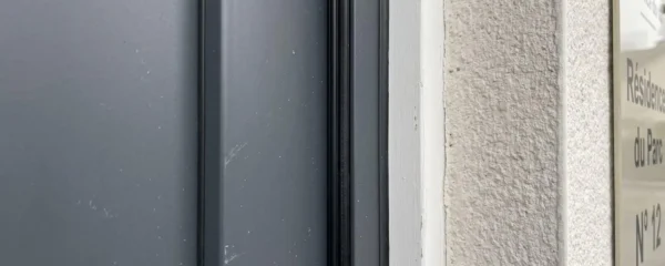 Gros plan sur le joint périphérique d'une porte d'entrée en aluminium anthracite vu depuis l'extérieur lors d'une réception de chantier